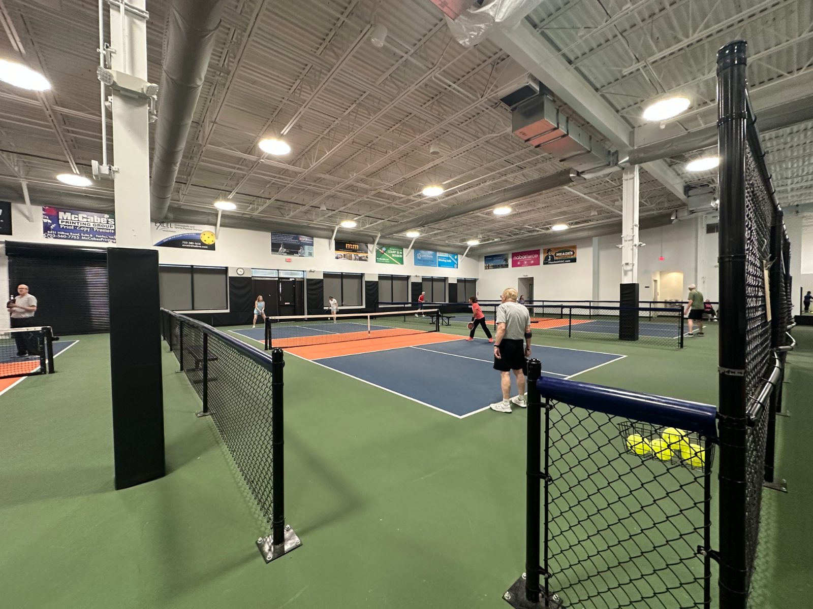 The indoor courts from the back — permanent net posts, ball caddy courtside, wide green run-off between courts.